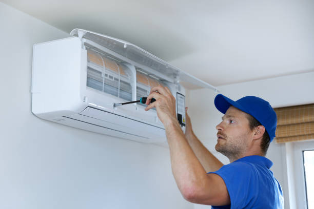A man wearing a blue shirt performs AC installation in Lauderhill, FL, focused on his task in a well-lit room.