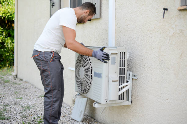 A man in a hard hat and blue overalls performs Goodman HVAC repair services in Tamarac, FL, focused on fixing an air conditioner.