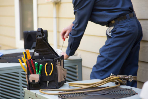 An HVAC technician in blue overalls performs maintenance on an air conditioner inside a Coral Springs home, representing the best HVAC maintenance and repair service near me.