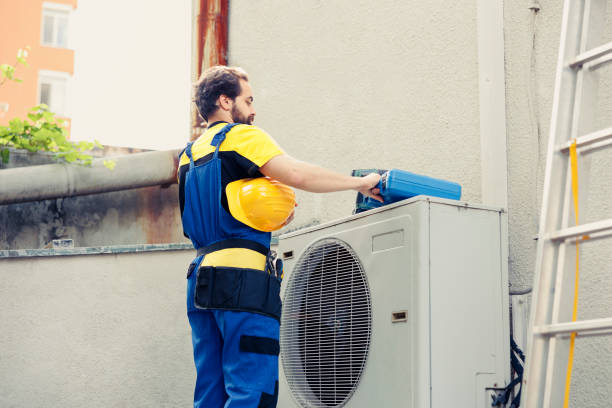 HVAC upgrade in Deerfield Beach FL – A technician in blue overalls and a yellow hard hat repairing an air conditioner