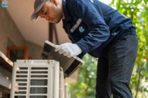 A technician wearing a blue shirt and white gloves is servicing an air conditioner, demonstrating expertise in HVAC repair and maintenance.