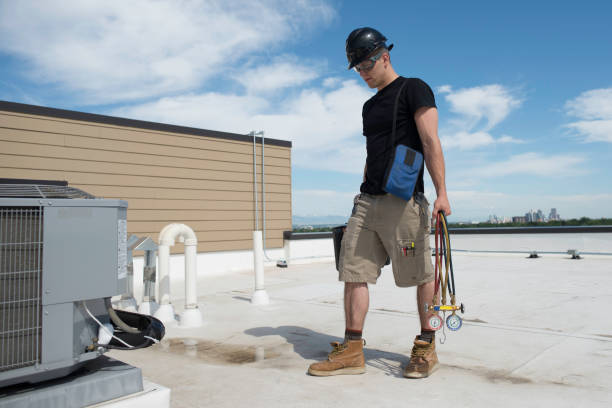 A man stands on a roof beside an AC condenser unit, overseeing the installation or maintenance work.