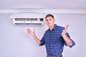 A man stands in front of a loud air conditioner, which is emitting a noticeable noise in the background.
