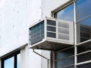 Sliding window AC mounted on a building wall, providing cooling for the interior space.