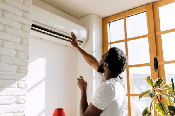 A man adjusts the air conditioner in his home, looking concerned as it is sign of AC Not Cooling.