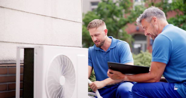 Two men in blue shirts perform emergency repairs on an air conditioner.