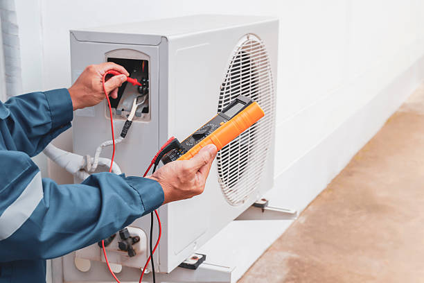 A man in a blue coat repairs an air conditioner, focusing on leak detection.