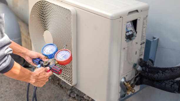 A technician in a blue coat is fixing an air conditioner, addressing a leak issue.