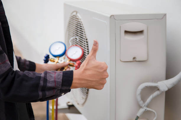 A technician in a blue coat is fixing an air conditioner, working on identifying a refrigerant leak.