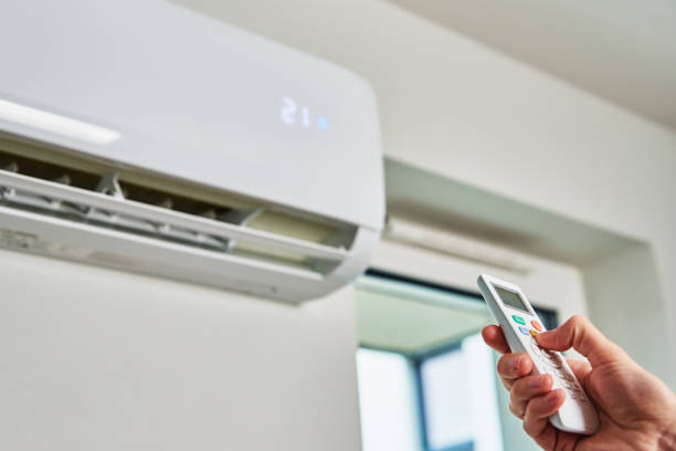 A person using a remote control to adjust a Reliable Air Conditioning unit in a well-lit room.