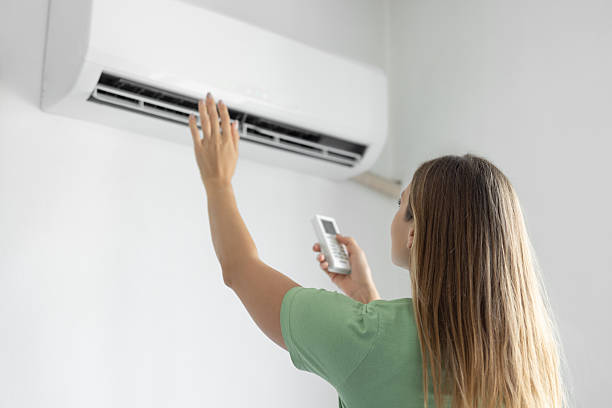 A woman holds a remote control, adjusting the air conditioner while discussing warm air issues in Margate, FL.