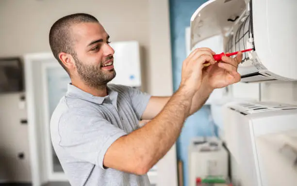 A man is repairing an air conditioner, focusing on the unit during an AC replacement process.